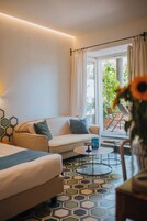 A modern hotel room with a sofa, a small round table, and a view of the outdoors.
