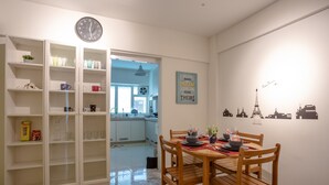 A dining area with a wooden table set for four, a kitchen in the background, and a wall with cityscape decals.