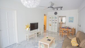 A modern living room with a flat-screen TV, a ceiling fan, a dining area with a table and chairs, and a white door.