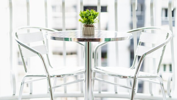 A balcony with a round table and two chairs, a small potted plant, and a grey rug with a white design.