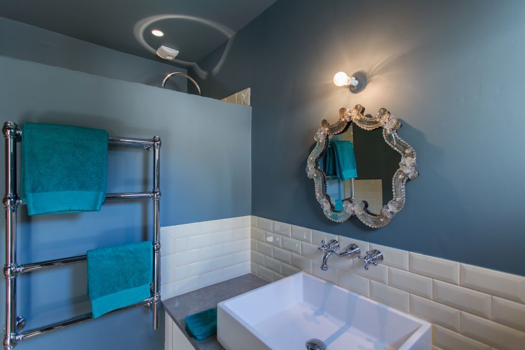 Une salle de bain avec une baignoire blanche, un porte-serviettes chromé orné de serviettes turquoise, un miroir décoratif et un mur recouvert de carreaux blancs.