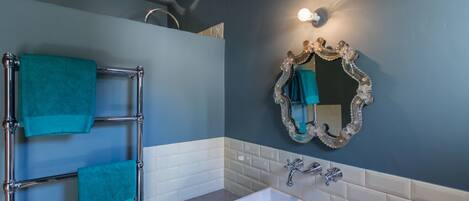 Une salle de bain avec une baignoire blanche, un porte-serviettes chromé orné de serviettes turquoise, un miroir décoratif et un mur recouvert de carreaux blancs.