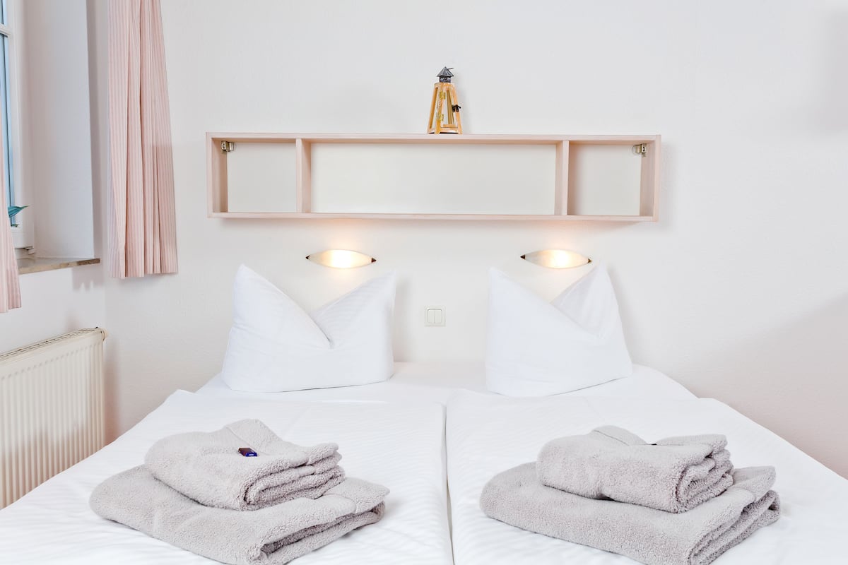 Une chambre d’hôtel avec deux lits, du linge de lit blanc, une étagère en bois au-dessus des lits et une petite lampe sur l’étagère.