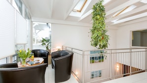 Un interior moderno con barandilla de vidrio, una planta colgante y una zona de estar con una mesa de centro.