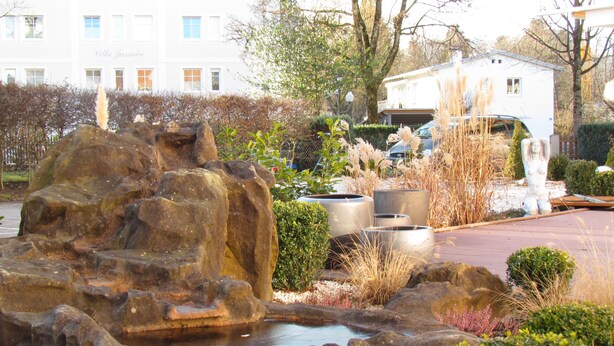 A landscaped garden with a rock feature, a small pond, and various plants. - Hotel Almrausch (Bad Reichenhall)