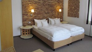 A double bed with a wooden headboard, two bedside lamps, a round side table, and a decorative wall piece. - Hotel Almrausch (Bad Reichenhall)