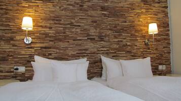 A hotel room with a stone wall headboard, two beds with white linens, and wall-mounted lamps.