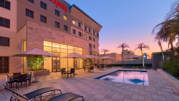 A hotel with a pool, outdoor seating, and palm trees. - StayEasy Lusaka (Lusaka)