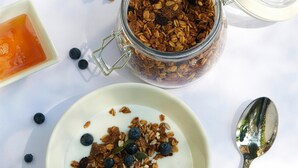 A glass jar filled with granola and blueberries, a small bowl of yogurt, and a spoon on a white surface. - StayEasy Lusaka (Lusaka)