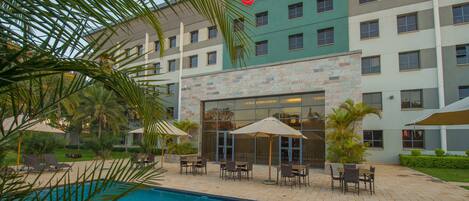 A hotel with a swimming pool, outdoor seating, and palm trees.