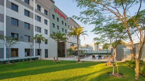 A hotel with a modern design, featuring a courtyard with palm trees, outdoor seating, and a swimming pool. - StayEasy Lusaka (Lusaka)