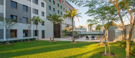 A hotel with a modern design, featuring a courtyard with palm trees, outdoor seating, and a swimming pool.