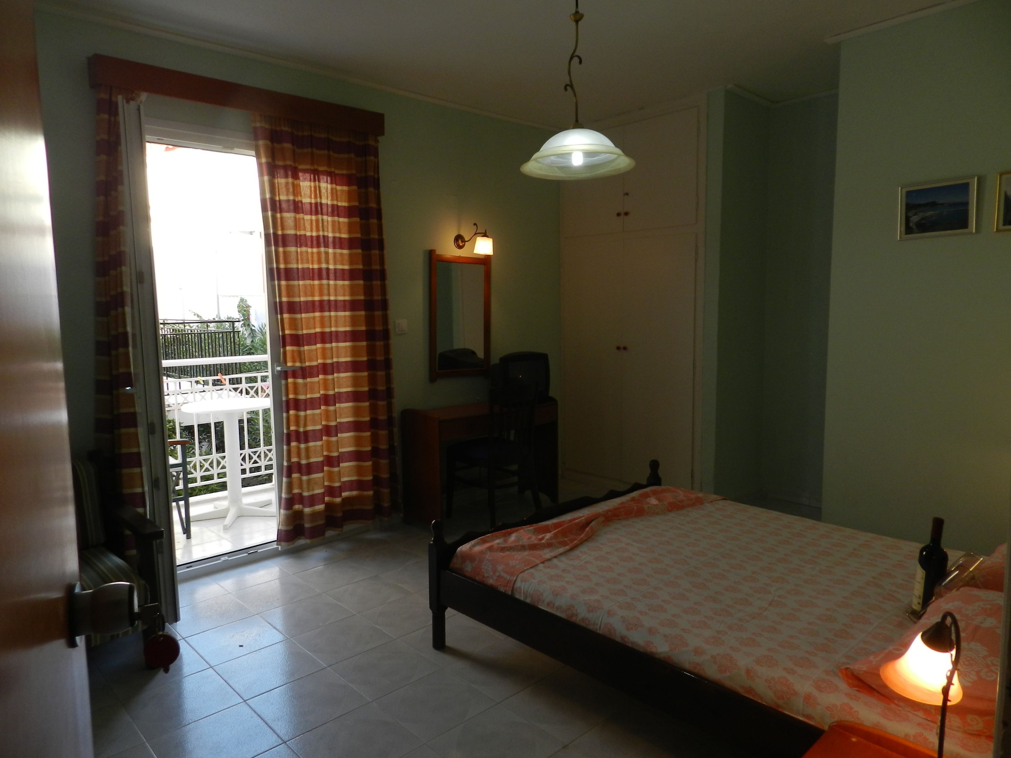 A bedroom with a bed, a desk, a chair, a wardrobe, and a balcony.