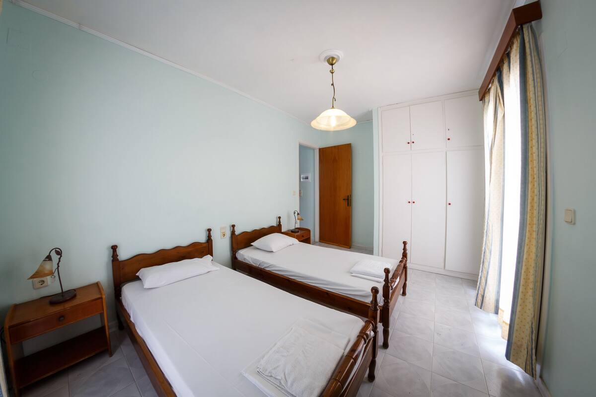 A bedroom with two wooden beds, a nightstand, a wardrobe, and a ceiling light.