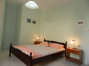 A bedroom with a wooden bed, two bedside tables with lamps, and light green walls. - Terra Azzura (Zakynthos)