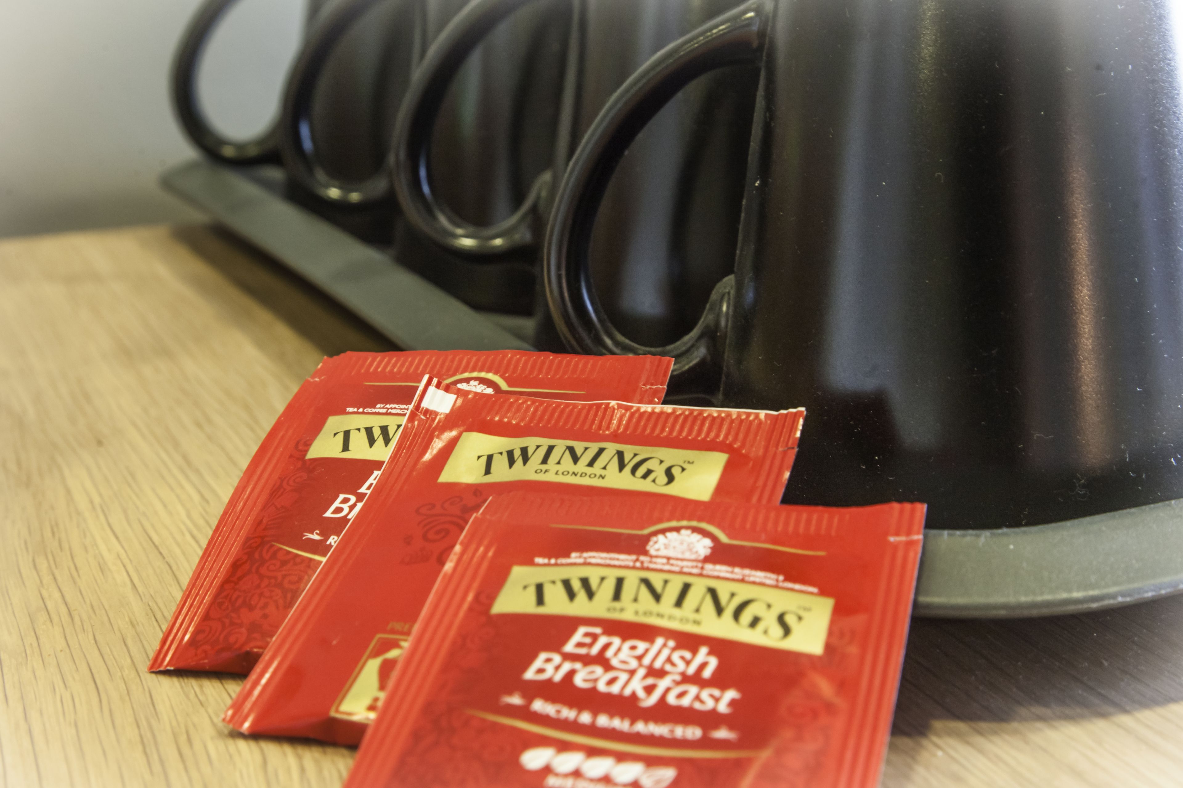 Una cafetera y tres sobres de té English Breakfast Twinings sobre una superficie de madera.