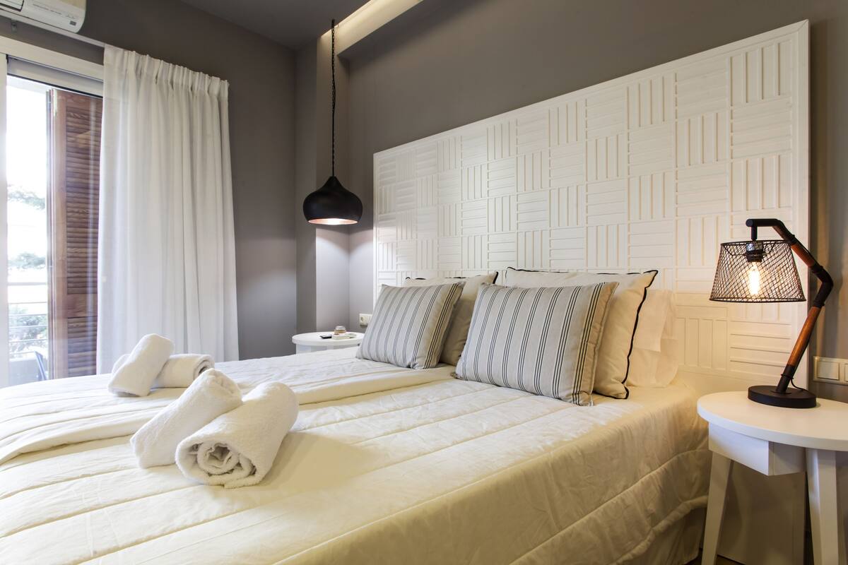 Een hotelkamer met twee bedden, een wit hoofdeinde, een nachtkastje met een lamp en een raam met gordijnen.