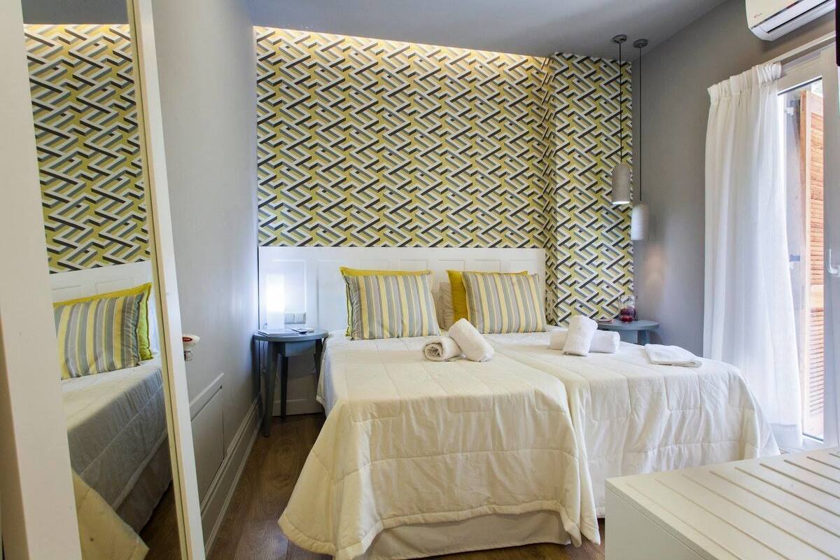 Hotelkamer met twee bedden, een nachtkastje, een lamp en een behang met patroon.