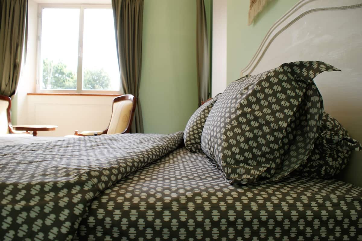 A neatly made bed with patterned bedding, a chair, and a window with curtains.