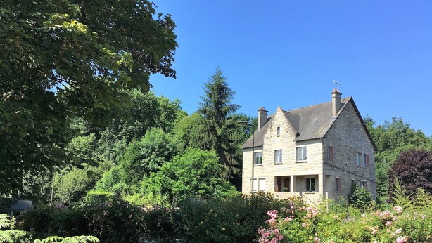 A stone house with a gabled roof, surrounded by lush greenery and flowering plants. - Les Voisins de l'Illet (Ercé-près-Liffré)