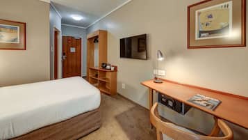 Une chambre d’hôtel avec un lit, un bureau avec une lampe, une télévision et une étagère sur laquelle se trouve une machine à café.