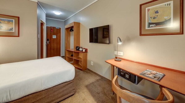 A hotel room with a bed, a desk with a lamp, a TV, and a shelf with a coffee maker.