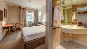 Habitación de hotel con cama, escritorio, silla y baño con lavamanos y espejo.