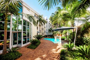 A resort with a swimming pool, palm trees, and a covered outdoor seating area. - StayEasy Pretoria (Pretoria)