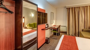 Habitación de hotel con dos camas, un escritorio, una silla, un espejo, un ventanal con cortinas y un perchero.