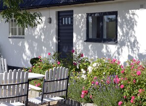 A white building with a black door and windows, a white picket fence, and a table with chairs.