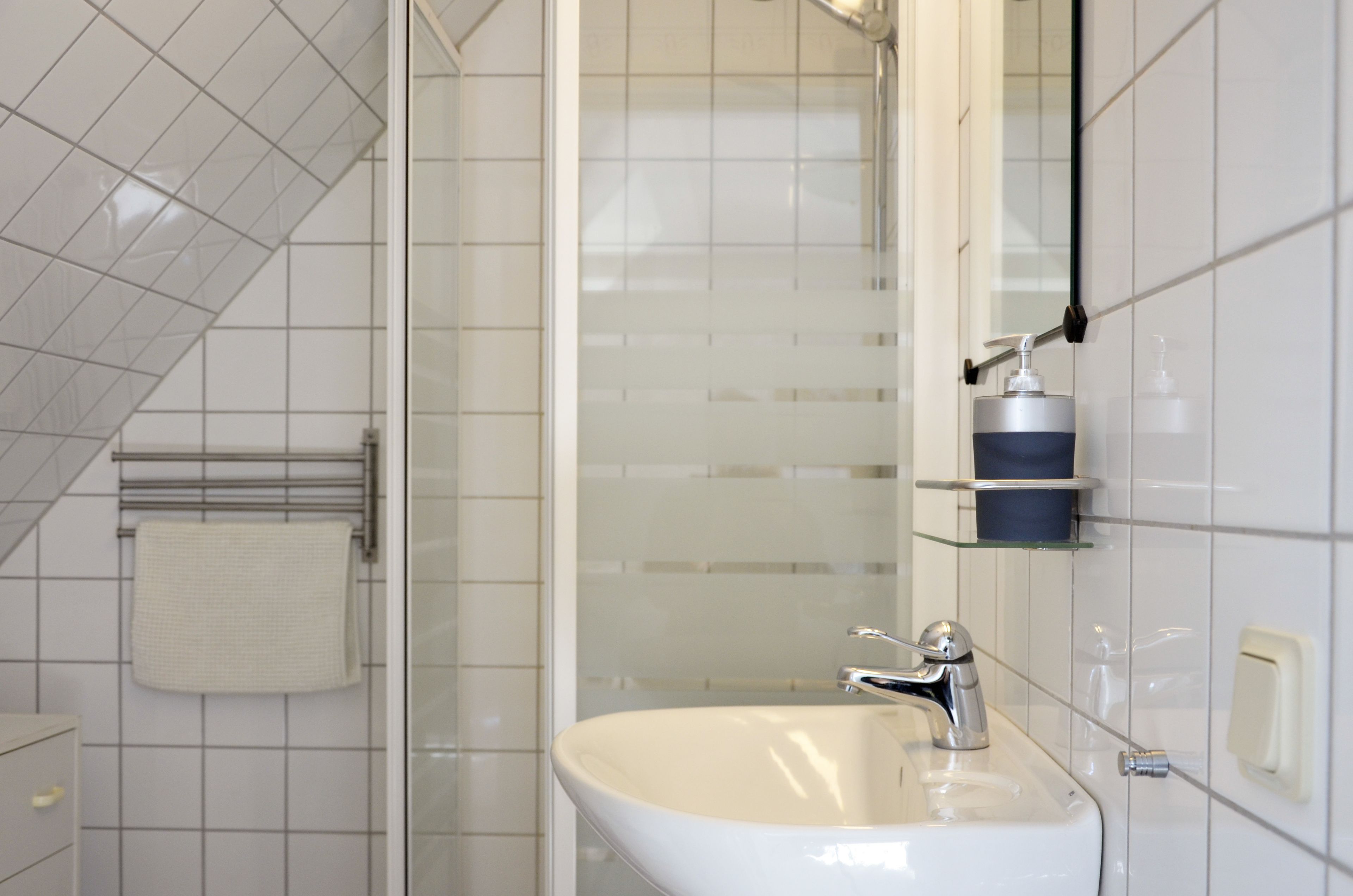 Un bagno moderno con un lavandino bianco, cabina doccia in vetro e porta asciugamani.