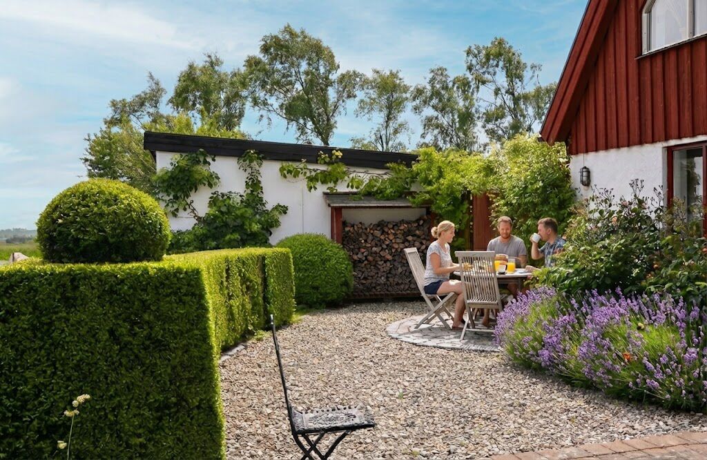 A patio with a table and chairs, surrounded by neatly trimmed hedges and a variety of plants.