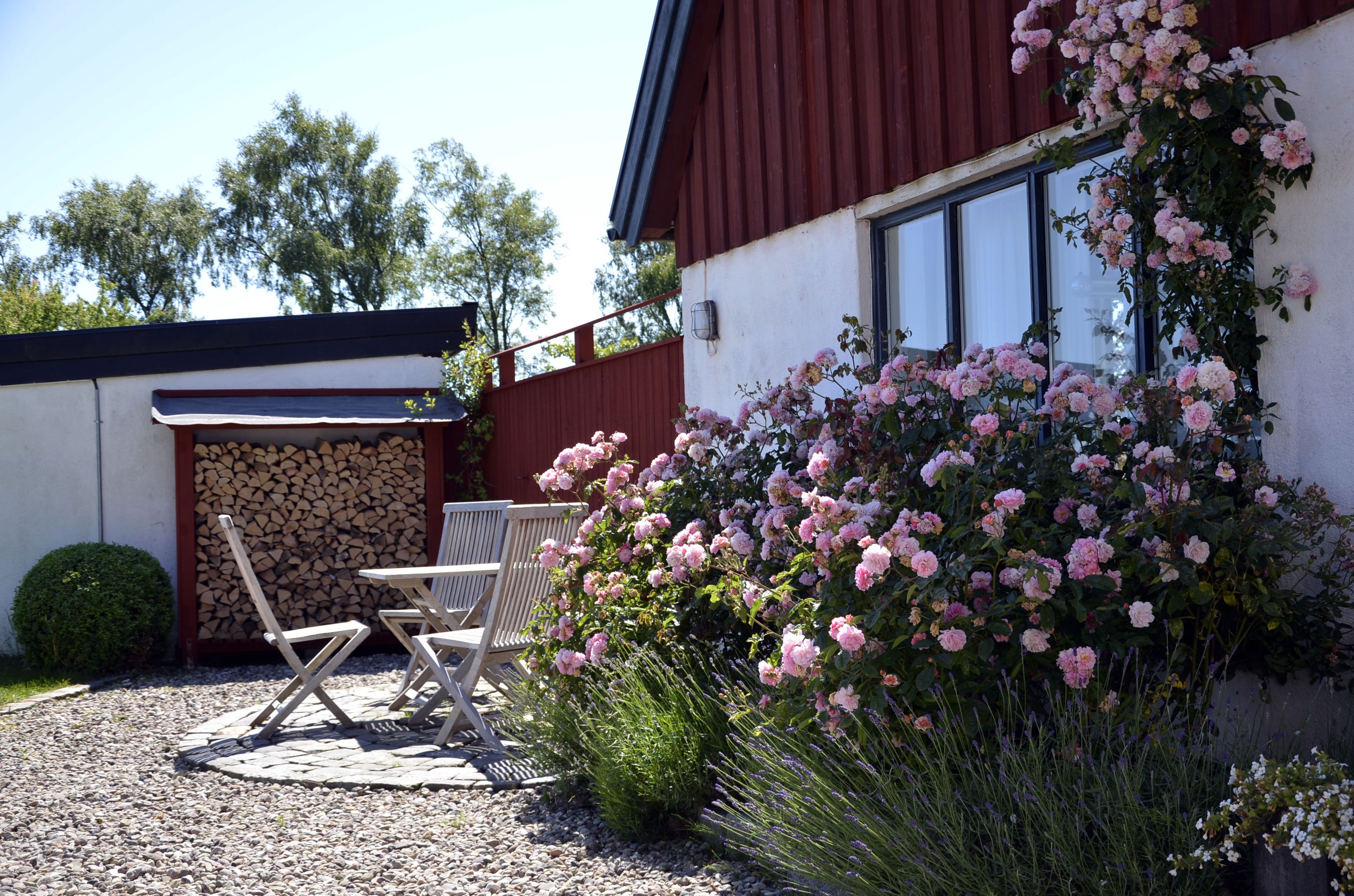 Un patio con una mesa y sillas, un cerco de madera y un jardín con flores rosadas.