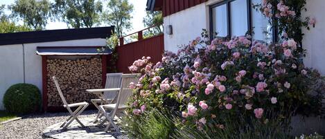 Un patio con una mesa y sillas, un cerco de madera y un jardín con flores rosadas.