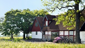 A traditional house with a sloped roof, surrounded by lush greenery and a field. - Torsborgs Gård (Simrishamn)