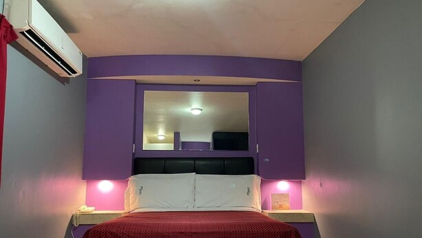 A bedroom with a bed, purple walls, a mirror above the bed, and two bedside lamps. - Motel Las Dunas (Mexicali)