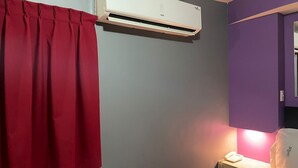 A room with a red curtain, a white air conditioning unit, a bedside table with a lamp, and a purple wall. - Motel Las Dunas (Mexicali)