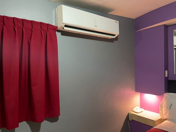 A room with a red curtain, a white air conditioning unit, a bedside table with a lamp, and a purple wall. - Motel Las Dunas (Mexicali)