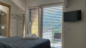 A bedroom with a bed, a TV mounted on the wall, and a window with blinds. - Italo-Svizzero (San Giacomo Filippo)