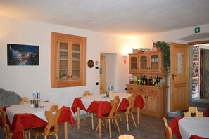 Un coin repas avec une table dressée pour quatre personnes, des chaises en bois, un buffet rempli de bouteilles et un tableau accroché au mur.