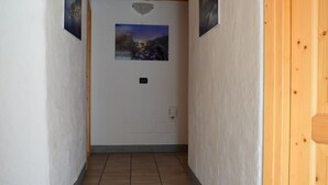 A hallway with wooden beams, white walls, and tiled flooring. There are two doors and two framed pictures on the walls. - Italo-Svizzero (San Giacomo Filippo)