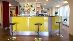 A bar area with a yellow counter, multiple stools, and a variety of bottles on shelves. - Hotel Tilmar (Rimini)