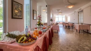 A hotel dining area with a long table set for breakfast, featuring a variety of fruits and beverages. - Hotel Tilmar (Rimini)