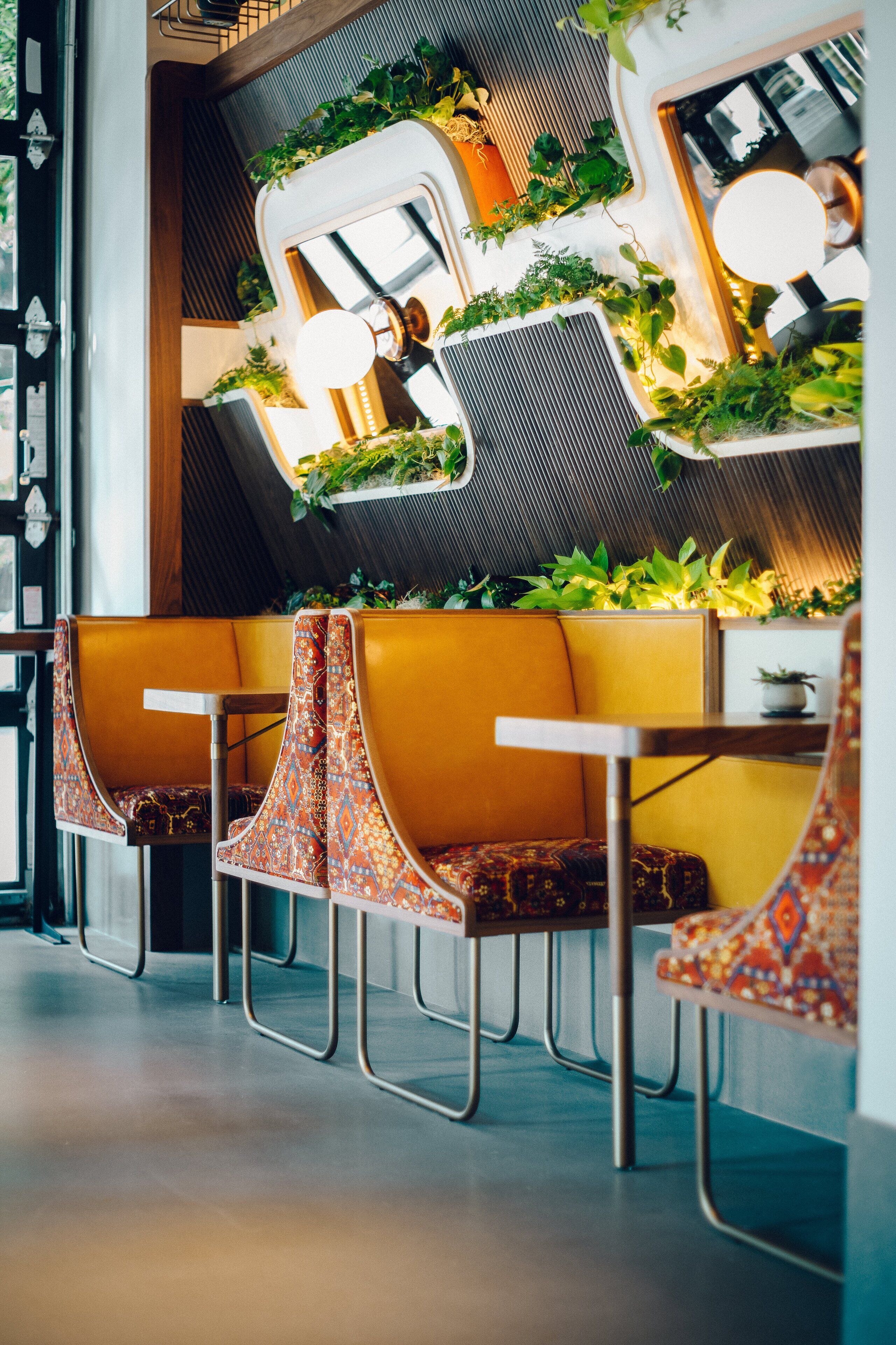 A modern restaurant interior with yellow booths, metal chairs, and green plants on the walls.