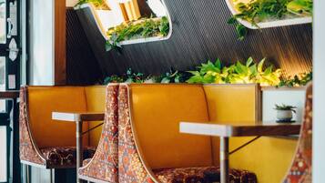 A modern restaurant interior with yellow booths, metal chairs, and green plants on the walls.