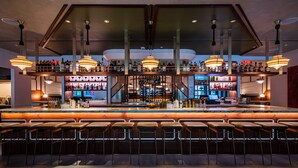 A bar area with multiple seating options, a well-stocked bar counter, and hanging pendant lights. - Eaton DC (Washington)