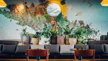 A cozy seating area with a mural, potted plants, and a wooden table.