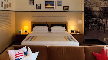 Une chambre d’hôtel avec un grand lit, un canapé marron et un mur orné de tableaux encadrés et d’une affiche.