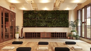 A yoga studio with wooden flooring, black yoga mats, and a wall of green plants.