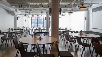 Una amplia sala de conferencias con varias mesas y sillas, ventanas grandes e iluminación de estilo industrial.